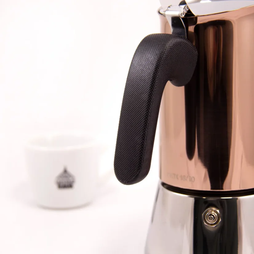 Cafetera Moka Bialetti New Venus para 6 tazas sobre fondo blanco con una taza de café, detalle del mango negro de la cafetera.