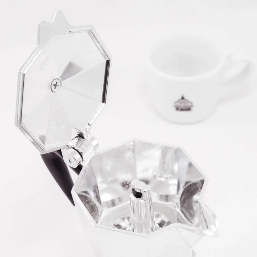 Silver Bialetti Moka Express pot, view into the interior of the pot, with a cup of coffee in the background