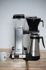 Silver Moccamaster coffee maker with a mug on a wooden table from the side