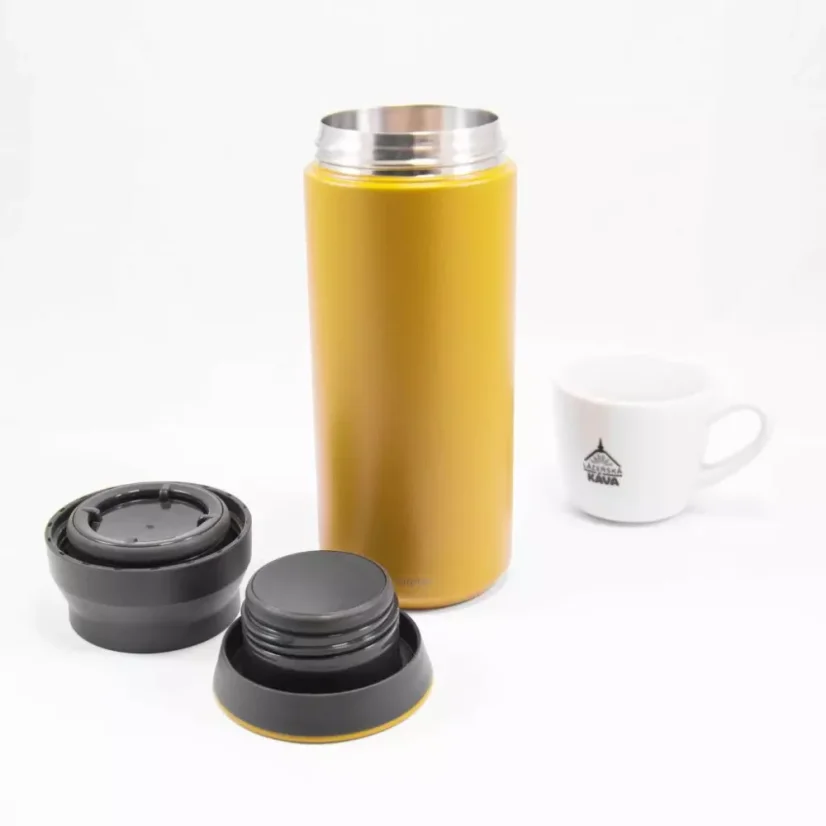 View of an unfolded yellow Kinto Travel Tumbler Coyote 500ml thermos alongside a porcelain cup of coffee.