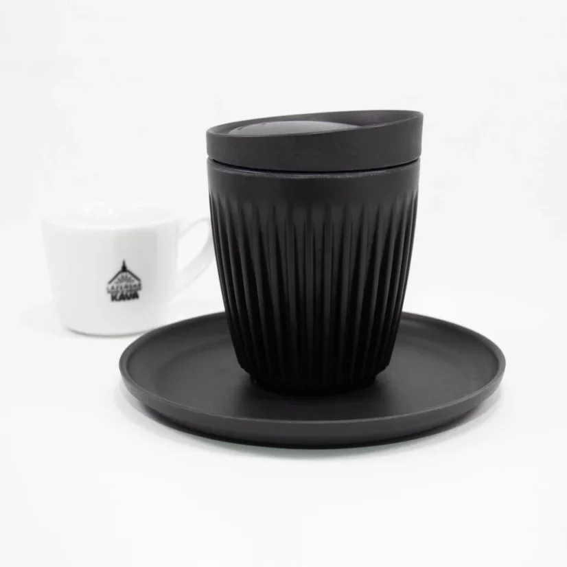 Black Huskee saucer with a cup and lid on a white background with a coffee cup.