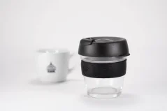 Szklany kubek termiczny z czarną pokrywką i czarnym uchwytem gumowym o pojemności 227 ml z filiżanką kawy.