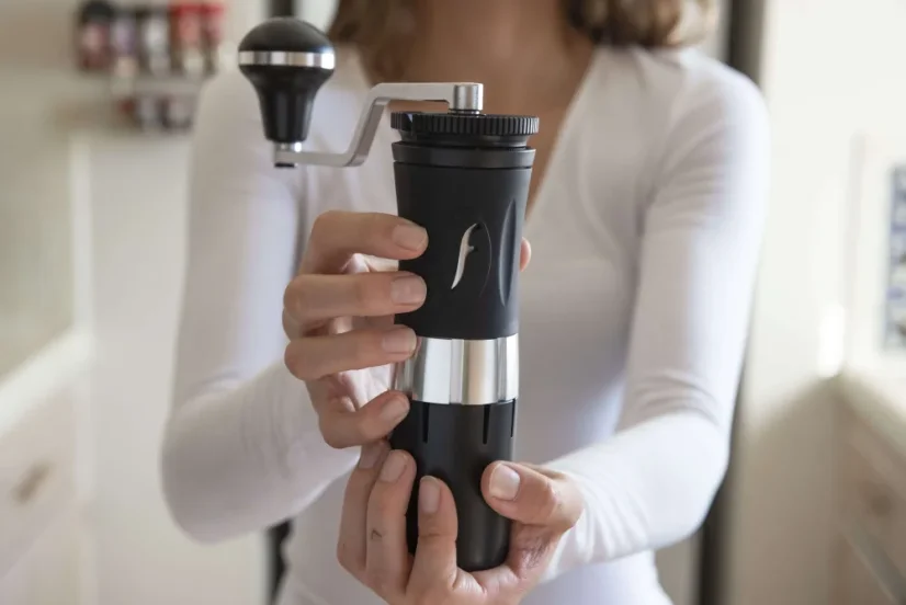 Baristka, ktorá drží čierny hliníkový ručný mlynček na kávu značky Flair Royale Grinder.