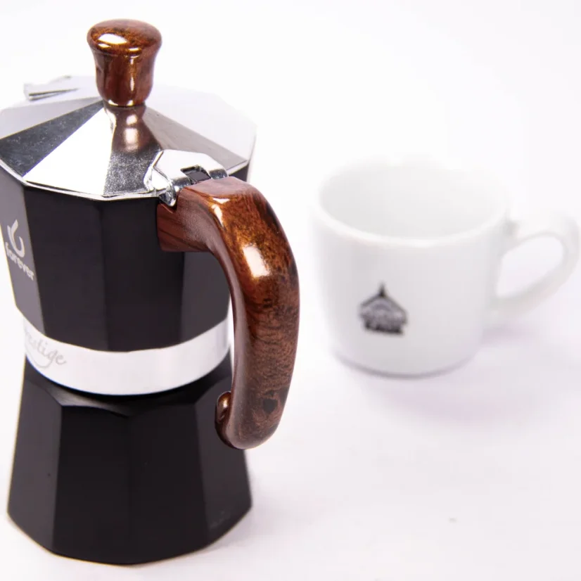 View of the back of the Forever moka pot with a wooden handle, with an espresso cup in the background.