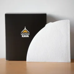 Weißer Papierfilter auf einem Holztisch, schwarze Schachtel mit Logo und weißem Hintergrund.