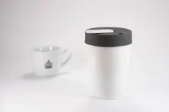 Porcelain thermal mug in white with a gray lid by Loveramics Nomad White 250ml with a cup of coffee in the background