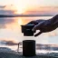 Trinity Zero held up by a hand away from a travel cup by the sea.