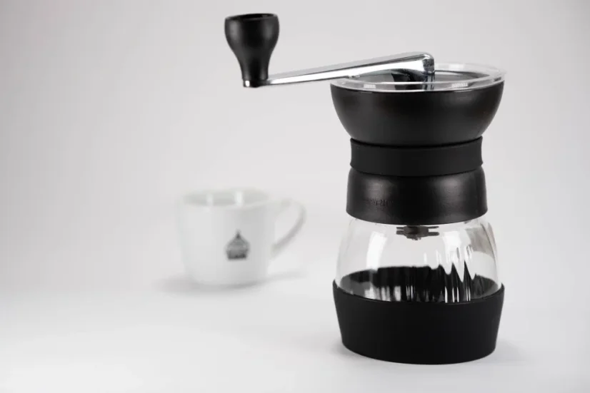 Black Hario Skerton Pro manual coffee grinder with a cup of coffee in the background