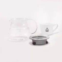 Jarra de vidrio para Hario V60 Range Server de 360 ml sobre una mesa blanca, acompañada de un inserto especial de goma y una taza de porcelana con logo.