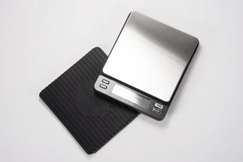 Balance digitale argentée sur un fond blanc avec un tapis en caoutchouc.