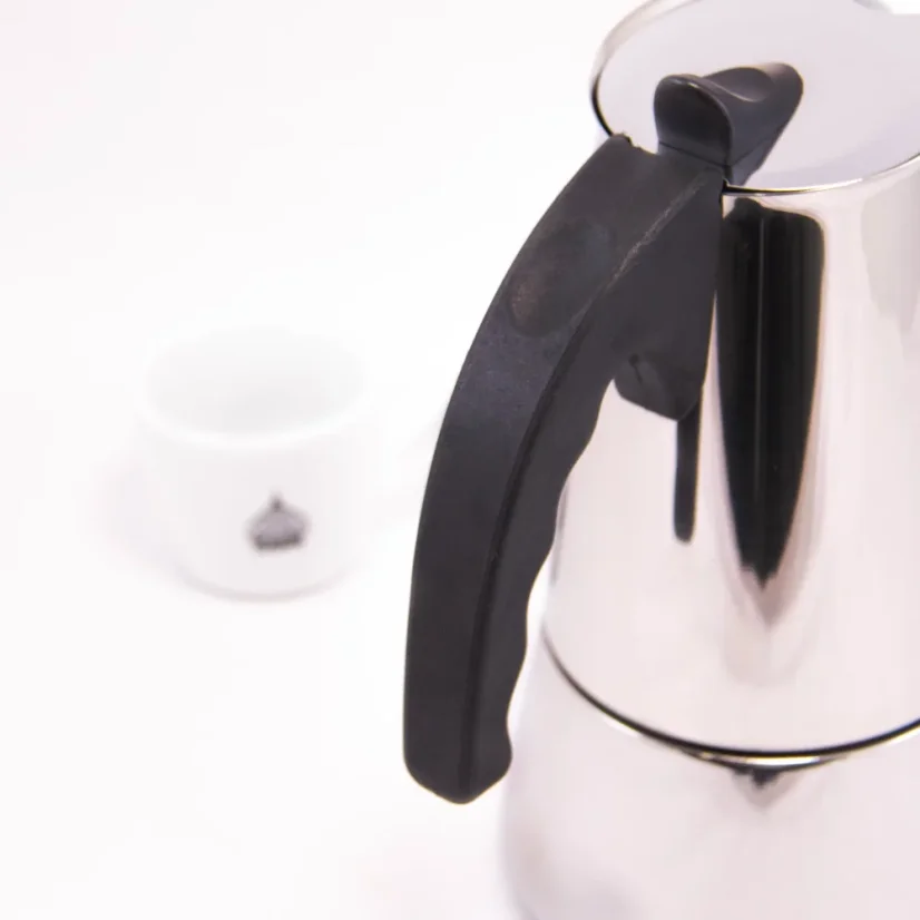Silver moka pot with a black handle for 10 cups on a white background with a cup of coffee, detail on the handle