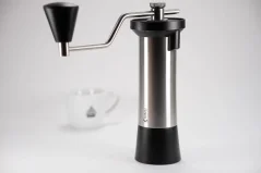 Molinillo de café manual de la marca Kinu, modelo Simplicity con una taza de café en el fondo.