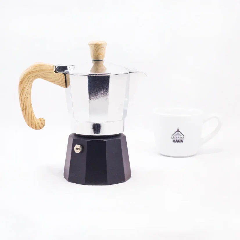 Cafetière Moka avec entonnoir noir pour l'eau et poignée en bois pour 2 portions de café, avec une tasse en porcelaine en arrière-plan.