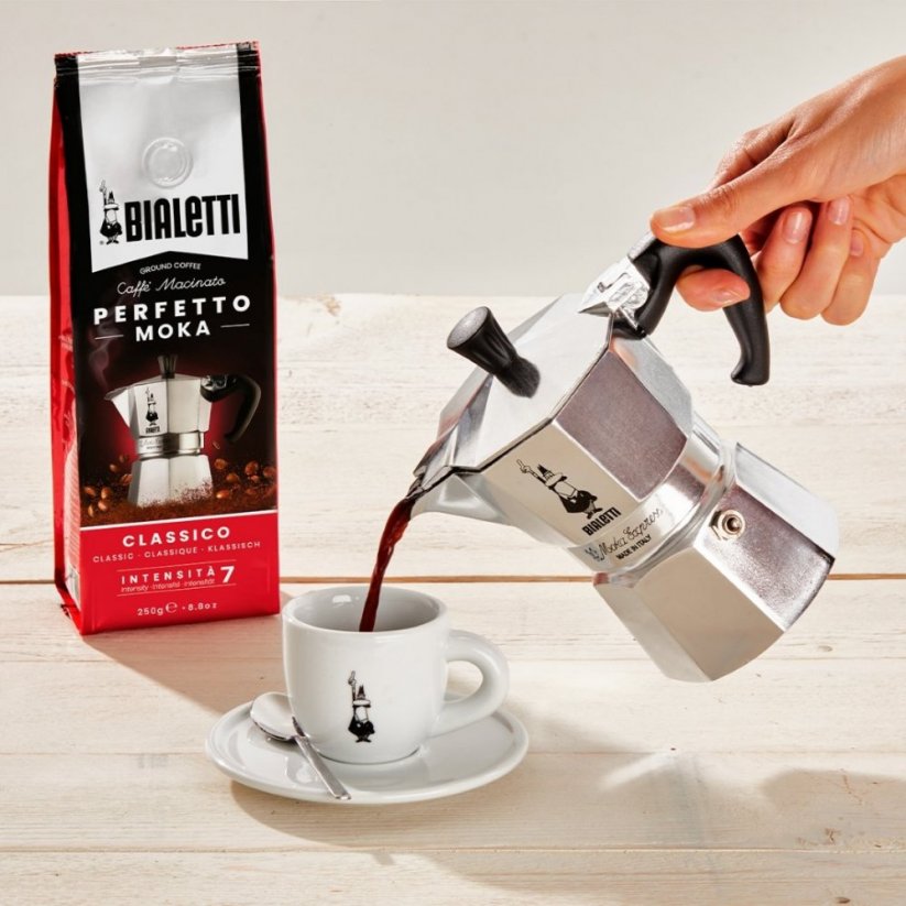 Pouring coffee prepared in a Bialetti Moka Express into a white cup with logo.