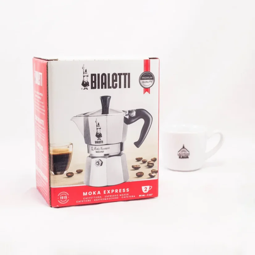 Cafetera Bialetti Moka Express plateada para 2 tazas en empaque original sobre fondo blanco con una taza de café.