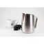 Cafetière symétrique en acier inoxydable pour le moussage du lait, posée sur une table avec des raisins rouges et une tasse décorée. Cafetière symétrique en acier inoxydable pour le moussage du lait, posée sur une table avec des raisins rouges et une tasse décorée.