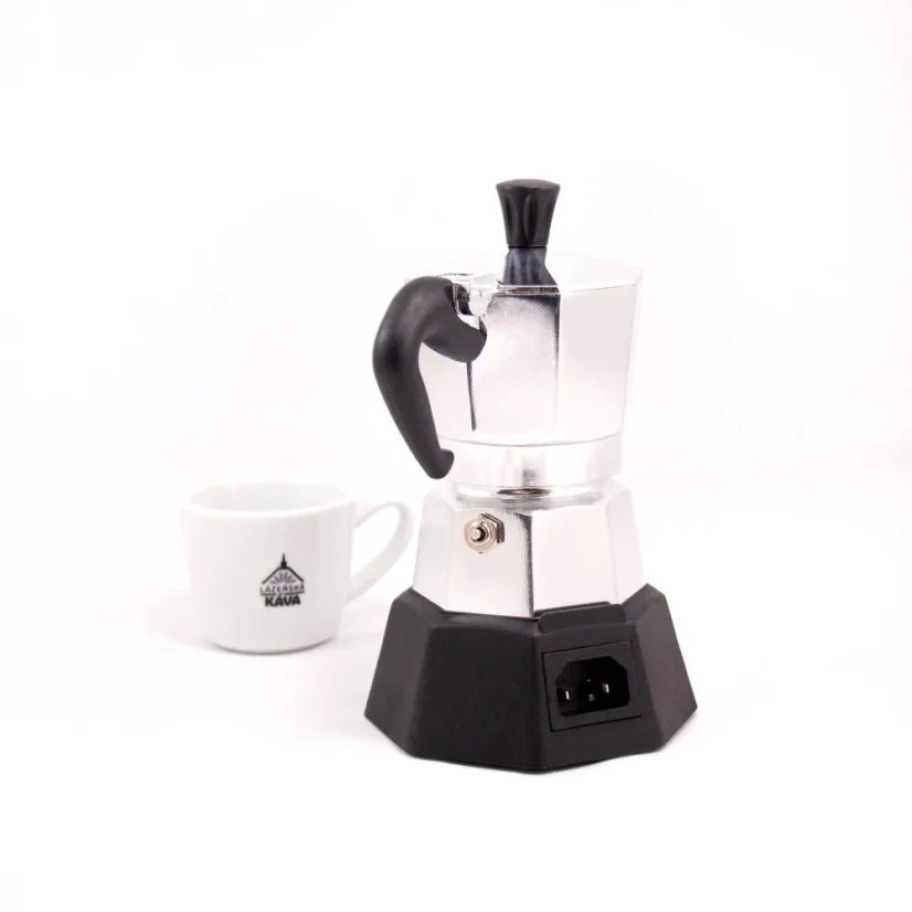 Rear view of a Bialetti Moka Elettrika Standard moka pot with a heating source and a porcelain cup of coffee in the background.