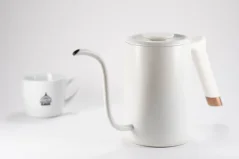 White Timemore Fish Pure Over electric kettle on a white background alongside a cup with decorative patterns.