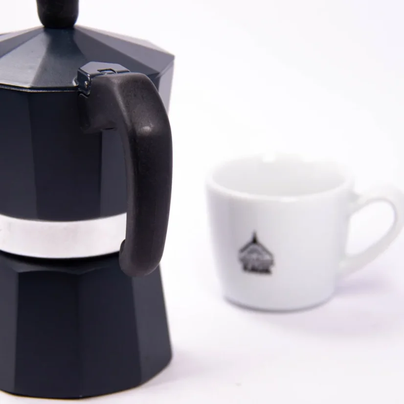Forever Prestige Noblesse Moka pot for 3 cups, detail on handle, with coffee in the background.