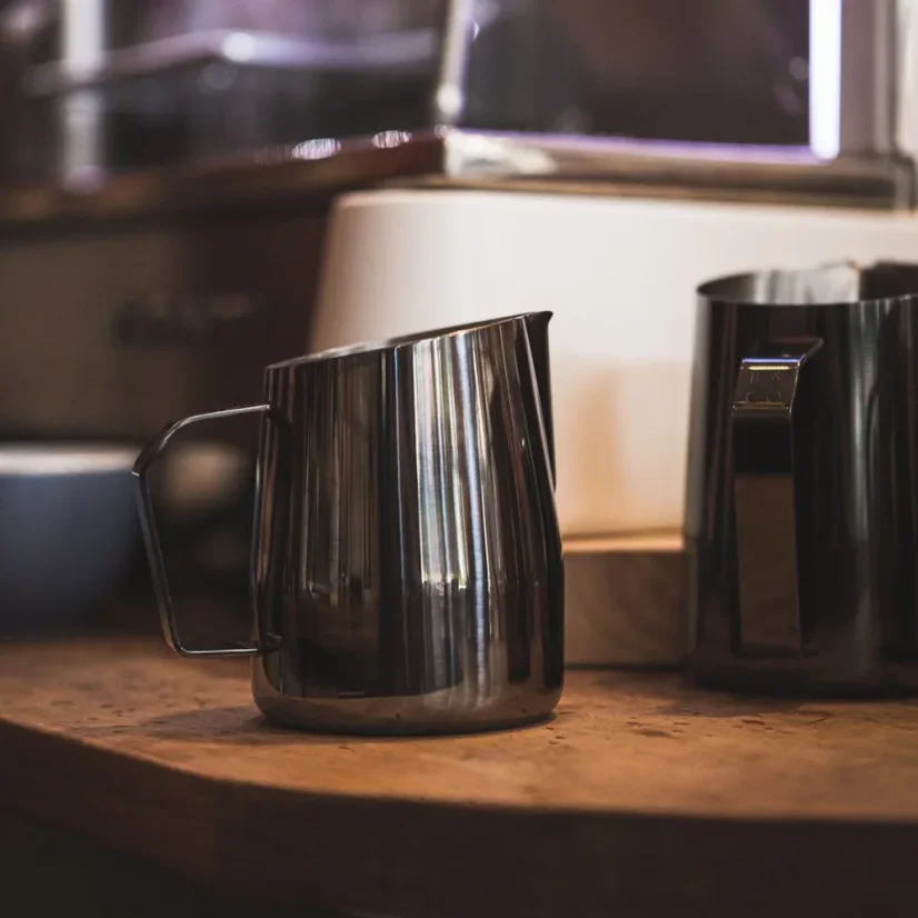 Stainless steel pitcher by Barista and Co Dial In Milk Pitcher 420ml in dark finish, paired with another pitcher