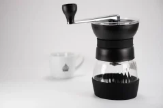 Macinacaffè manuale nero Hario Skerton Pro con una tazza di caffè sullo sfondo.