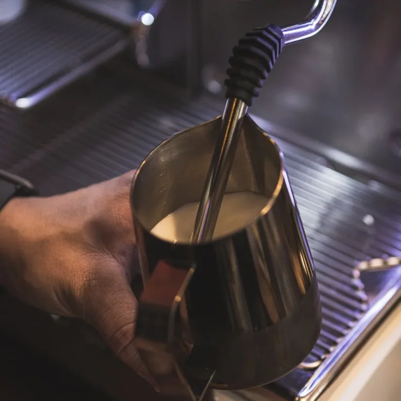 Whisking milk in a stainless steel pitcher by Barista and Co Dial in Milk Pitcher 420ml in dark finish using a coffee machine nozzle