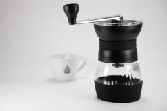 Čierny ručný mlynček Hario Skerton Pro s šálkom kávy v pozadí