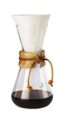 Chemex en verre avec une tête allongée, poignée en bois et une lanière en cuir, incluant un filtre en papier blanc et du café préparé.