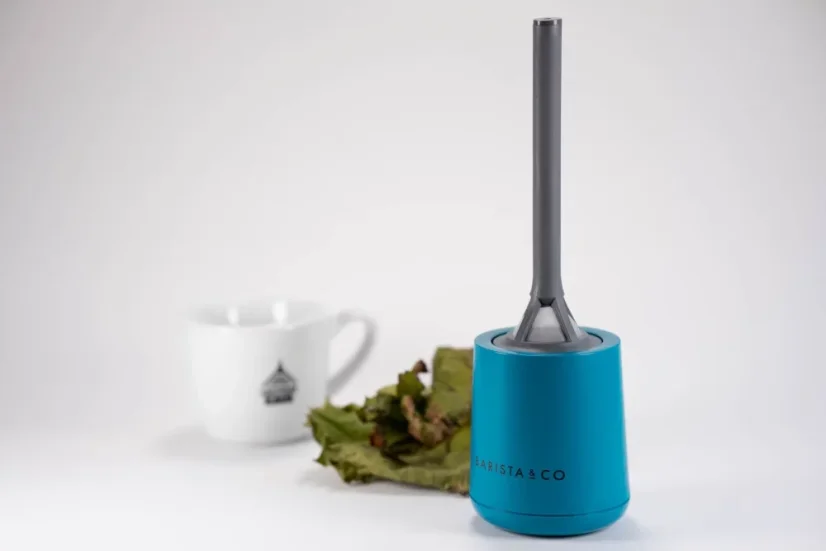 Grey plastic strainer with a blue holder and a porcelain cup with a plant in the background.