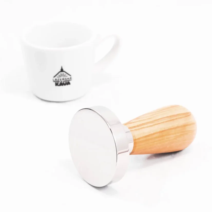 Detail of a tamper with an olive wood handle, with coffee in the background.