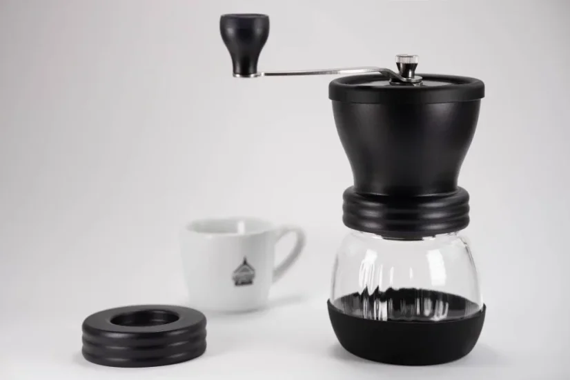 Hario Skerton Plus black manual coffee grinder with a cup of spa coffee