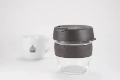 Gobelet thermique en verre de 227 ml avec un couvercle gris et une bande de maintien en caoutchouc gris sur fond blanc avec une tasse de café.