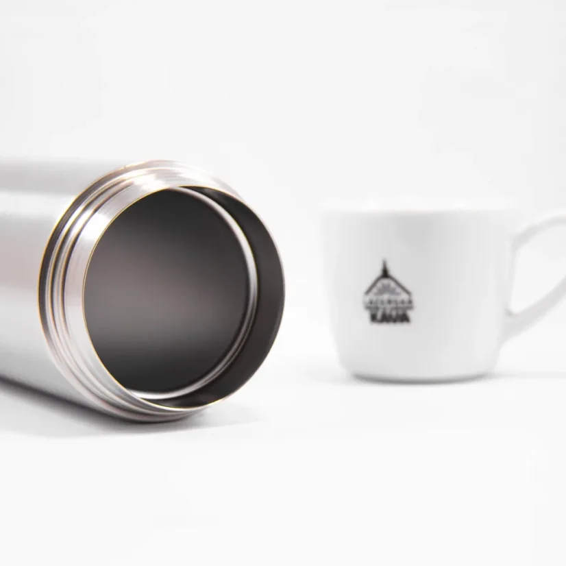 Liegender Thermobecher Kinto ohne Deckel auf weißem Hintergrund mit einer Tasse Kaffee.