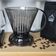 Dripper de plástico gris sobre una mesa de madera con granos de café y un paquete de café con logo.