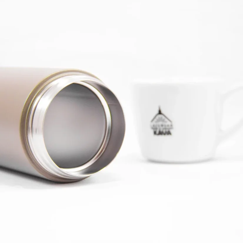 View into the Kinto Travel Tumbler Khaki 350ml thermos on a white table alongside a cup of coffee.