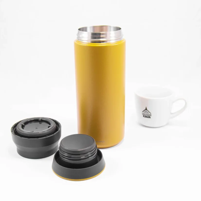 Pohľad na rozloženú žltú termosku Kinto Travel Tumbler Coyote 500ml spolu s porcelánovým šálkom kávy.