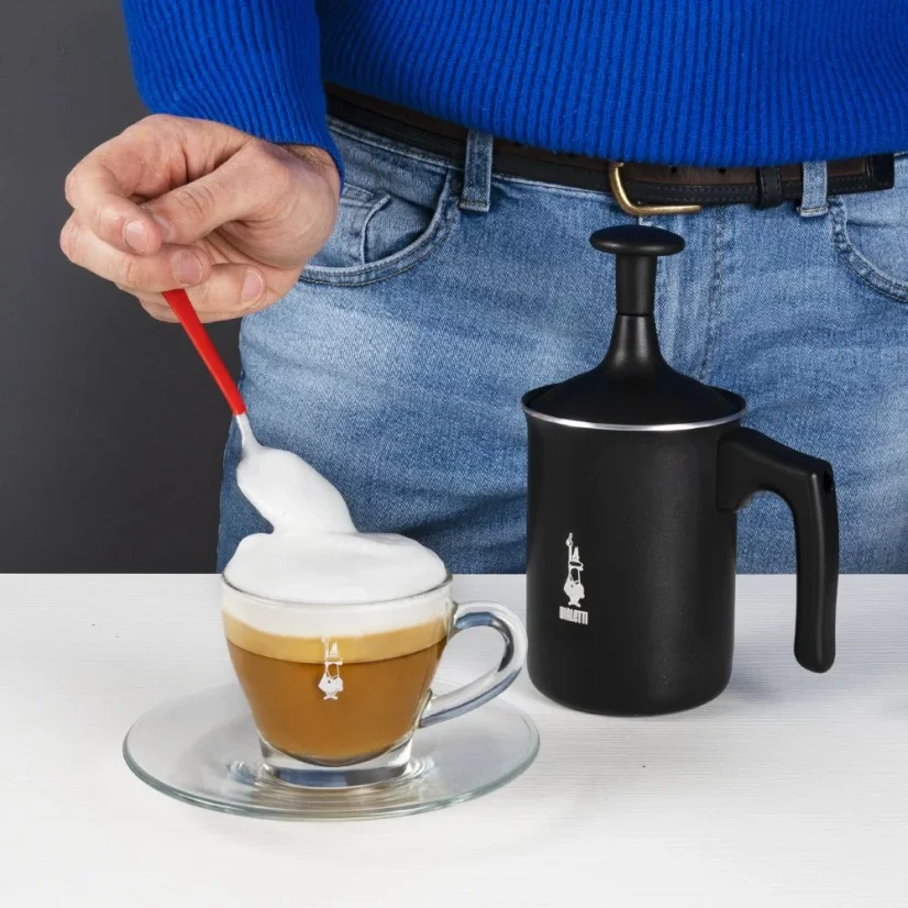 Sort mælkeskummer fra Bialetti Tuttocrema 330ml med en barista i baggrunden, der tilsætter pisket mælk til en Cappuccino.