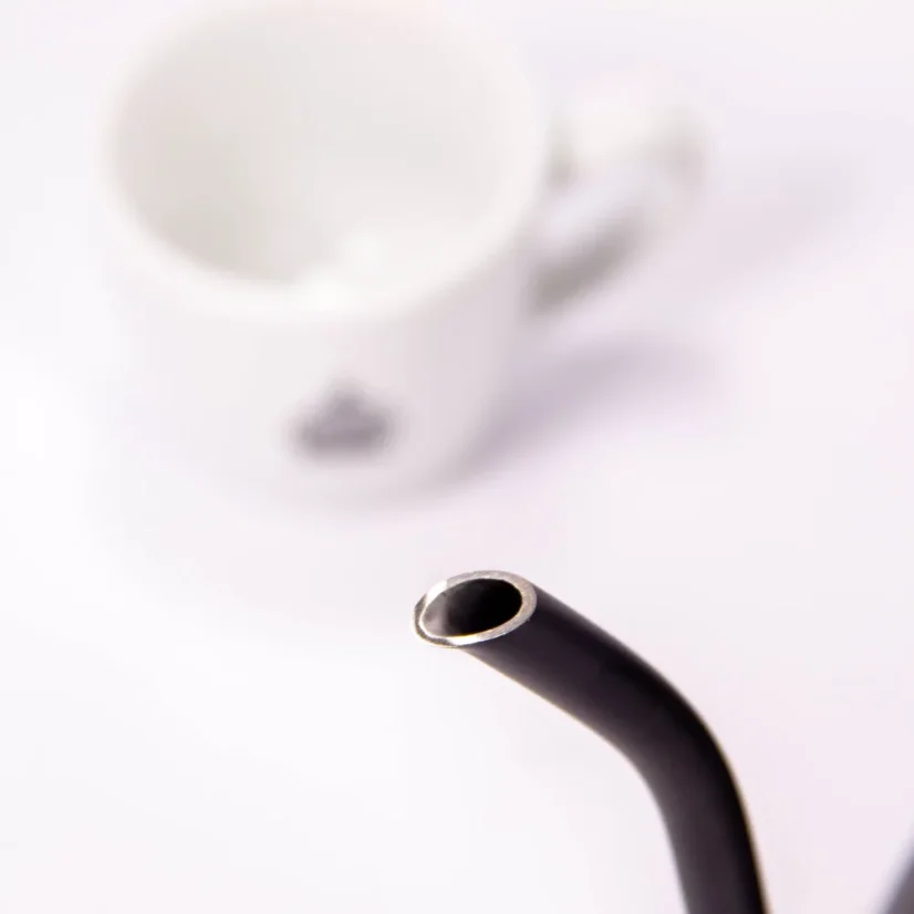 Bouilloire électrique noire sur un fond blanc avec une tasse de café, détail sur le col de cygne de la bouilloire.