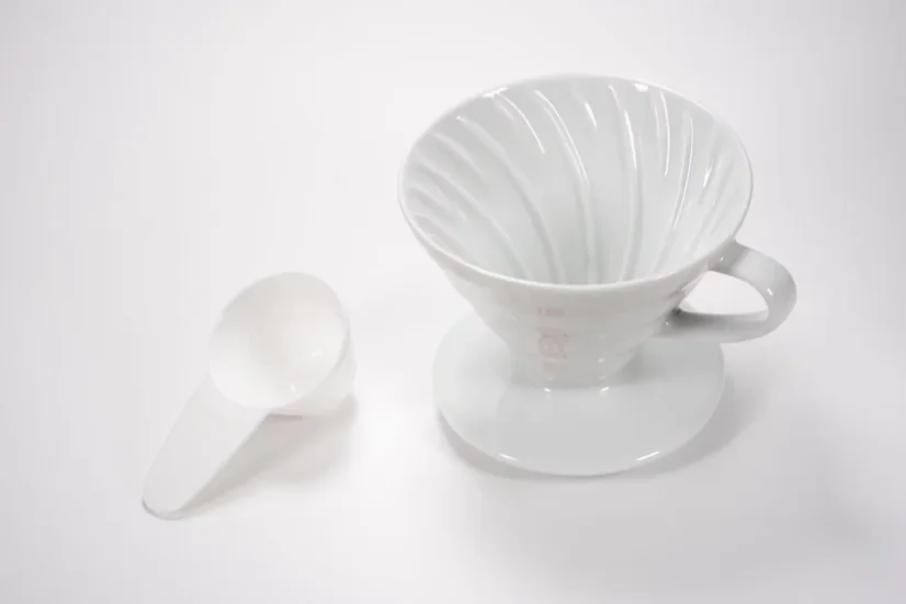 White ceramic Hario V60-01 dripper with a plastic coffee doser on a light background.