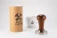 Heavy Temper with a diameter of 58.4 mm with a wooden handle on the table, along with the original packaging and a porcelain cup with coffee motifs.