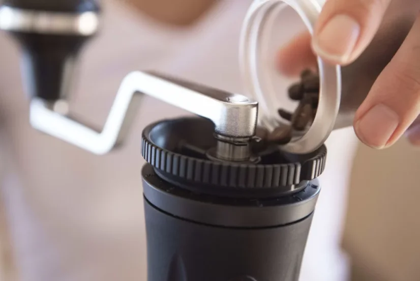 Barista pouring coffee into a black Flair Royale Grinder manual coffee grinder.