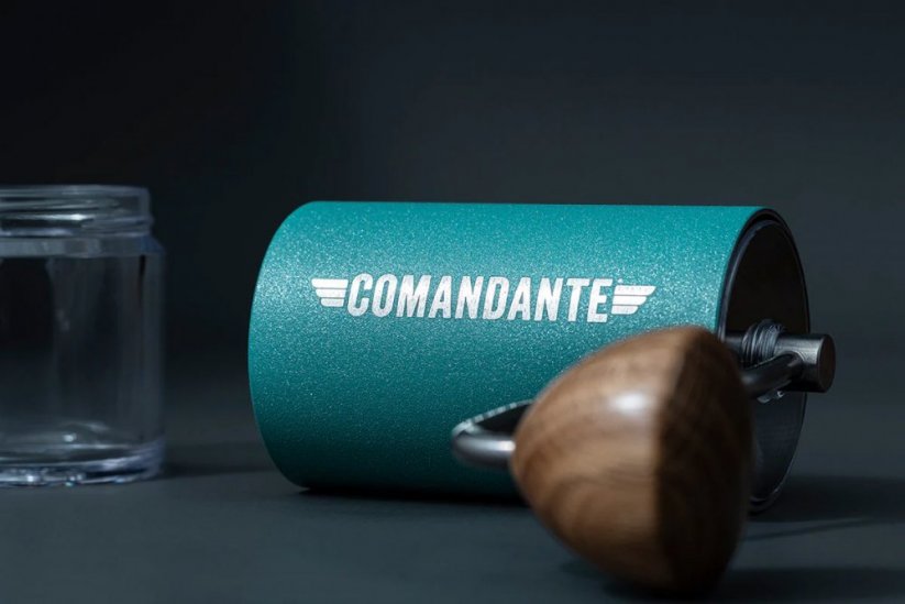 Hand grinder Comandante in Alpine Lagoon colour in front of a black background with separate collection container for ground coffee.