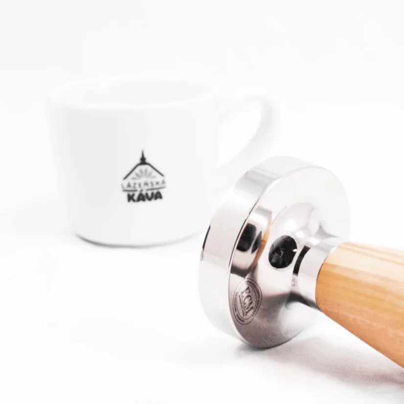 Detail tampéra s rukoväťou z olivového dreva s kávou v pozadí.