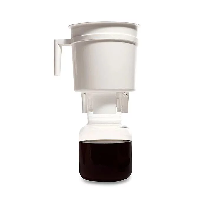 Systém Toddy Cold Brew s bielou plastovou nádobou na filter a prekvapkávanou kávou vo spodnej sklenenej časti na bielom pozadí.