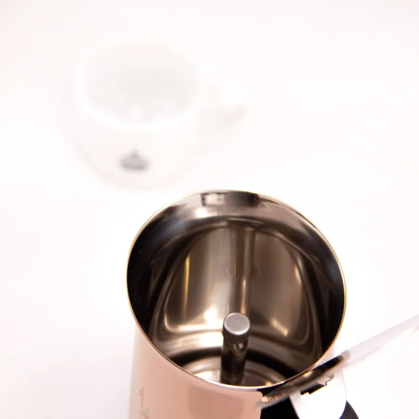 Moka konvička Bialetti New Venus pre 6 šálkov na bielom pozadí so šálkom kávy, pohľad do vnútornej časti konvičky.