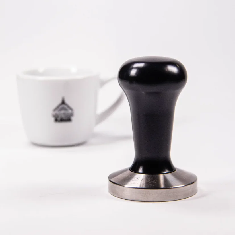 Tamper 58,4 mm s čiernou rukoväťou a šálka na kávu.