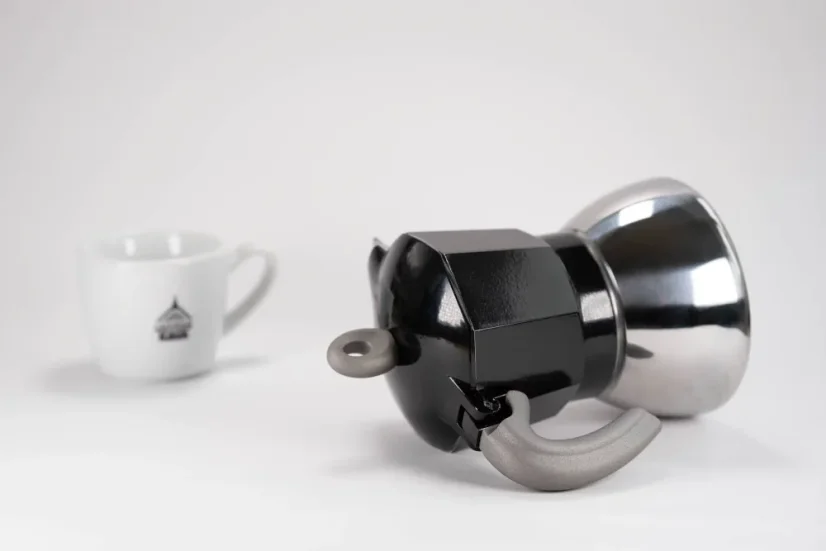 Practical handle of an aluminum moka pot suitable for induction by the Italian brand Bialetti, composed with a cup featuring a logo.