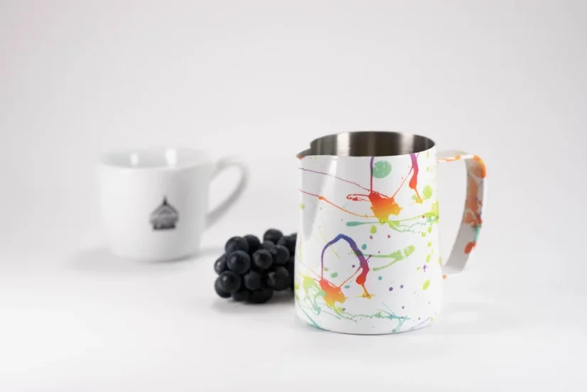 Stainless steel white pitcher with colorful splashes for milk frothing by Barista Space Splash, paired with a cup with a red grape wine.