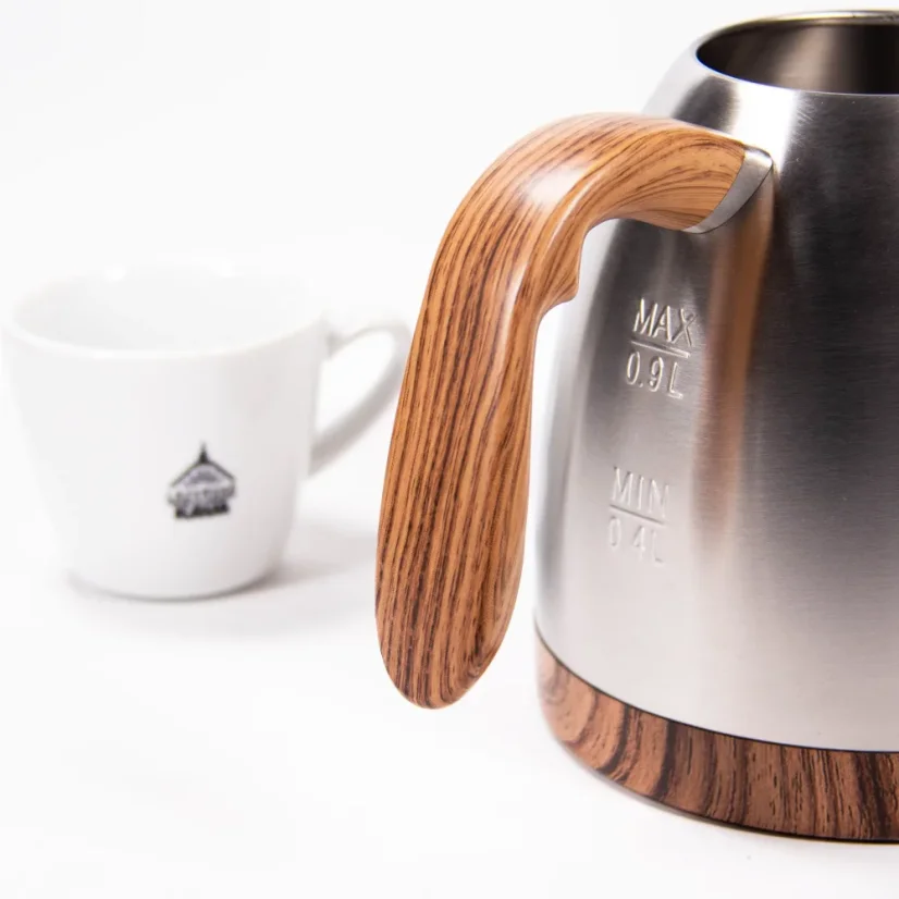 Bouilloire électrique argentée, détail sur la poignée en bois sur fond blanc avec une tasse de café