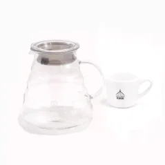 Carafe en verre Hario pour V60 avec un insert en caoutchouc spécial, posée sur une table blanche avec une tasse blanche. Carafe en verre Hario pour V60 avec un insert en caoutchouc spécial, posée sur une table blanche avec une tasse blanche.